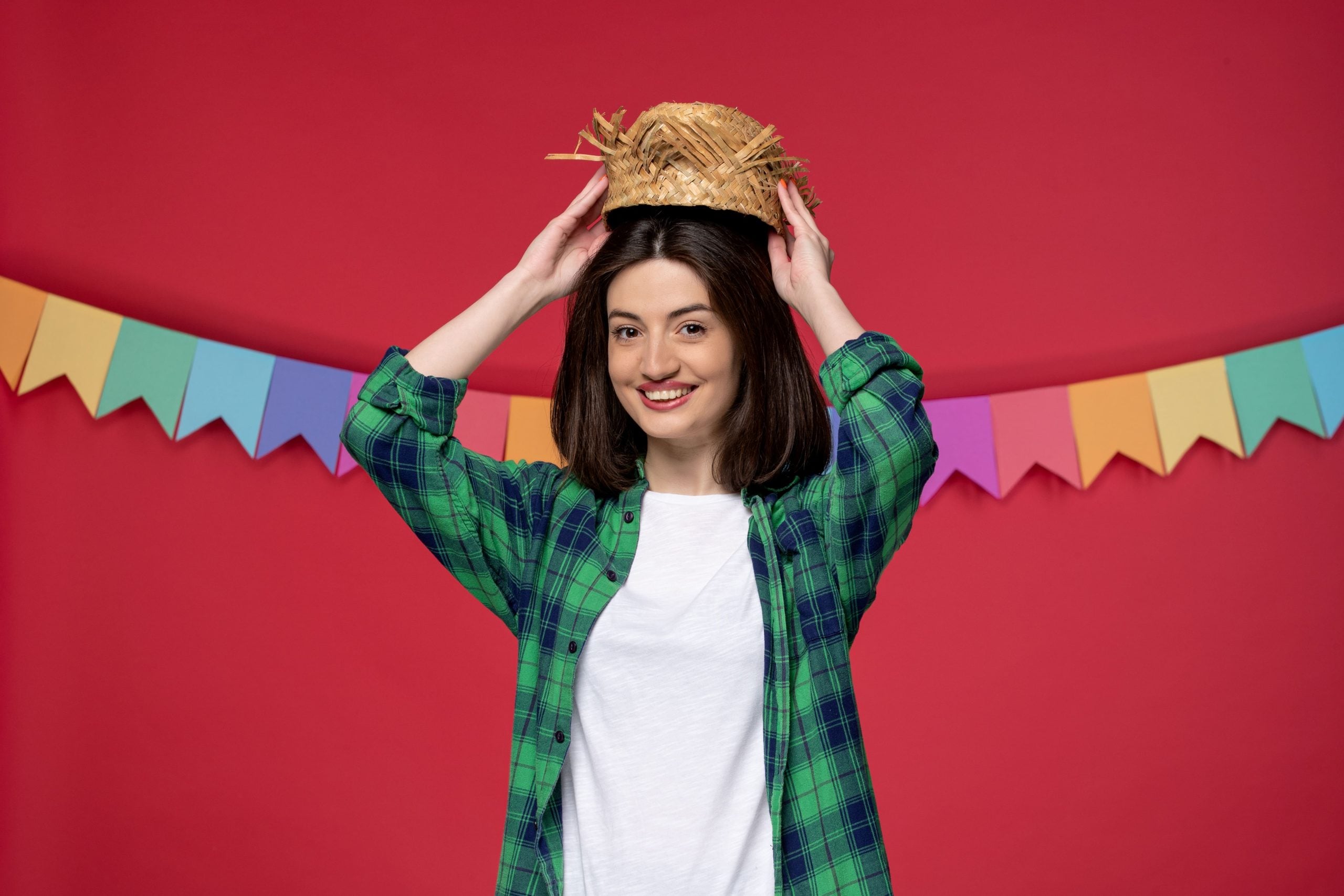 Mulher usando camisa xadrez verde e chapéu de palha em fundo de festa junina.
