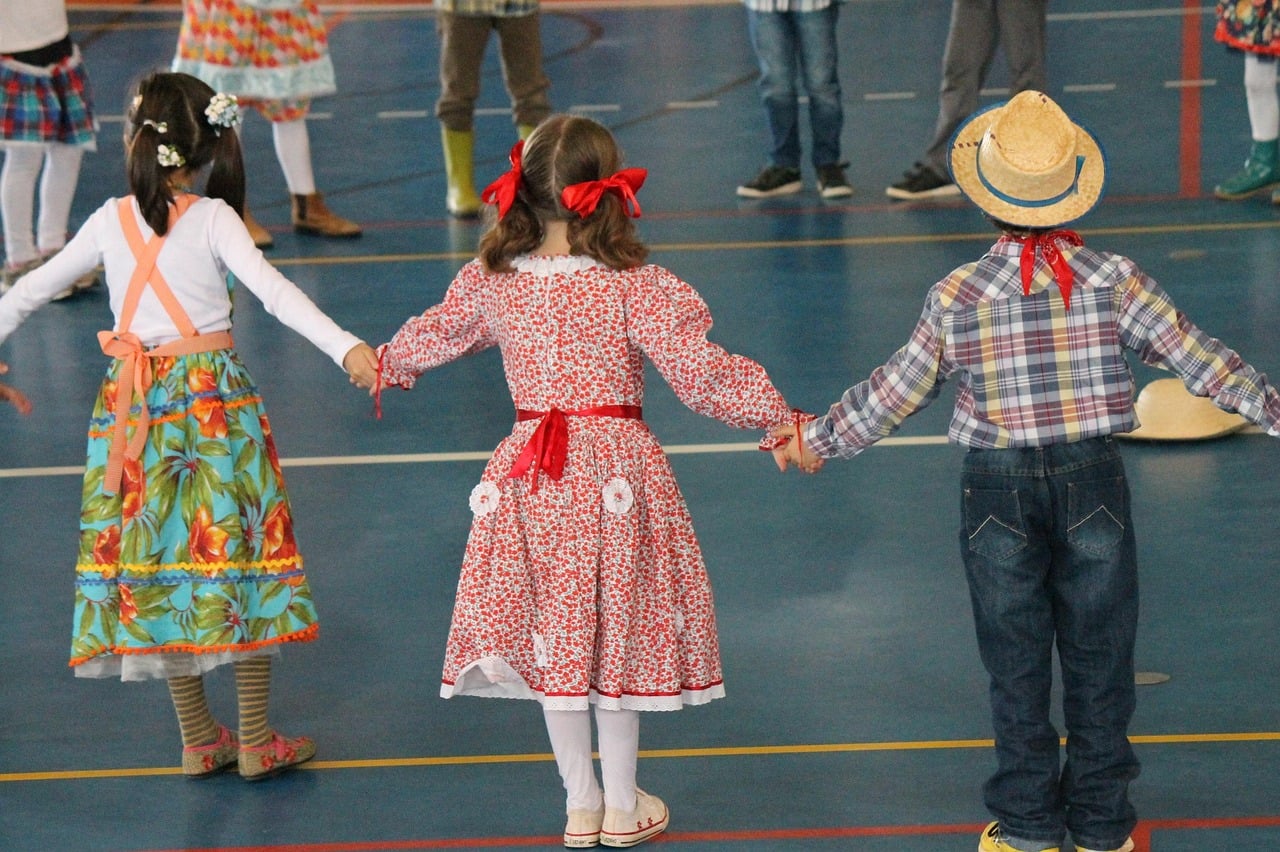 Crianças vestidas com trajes típicos de festa junina participando de roda em comemoração escolar.
