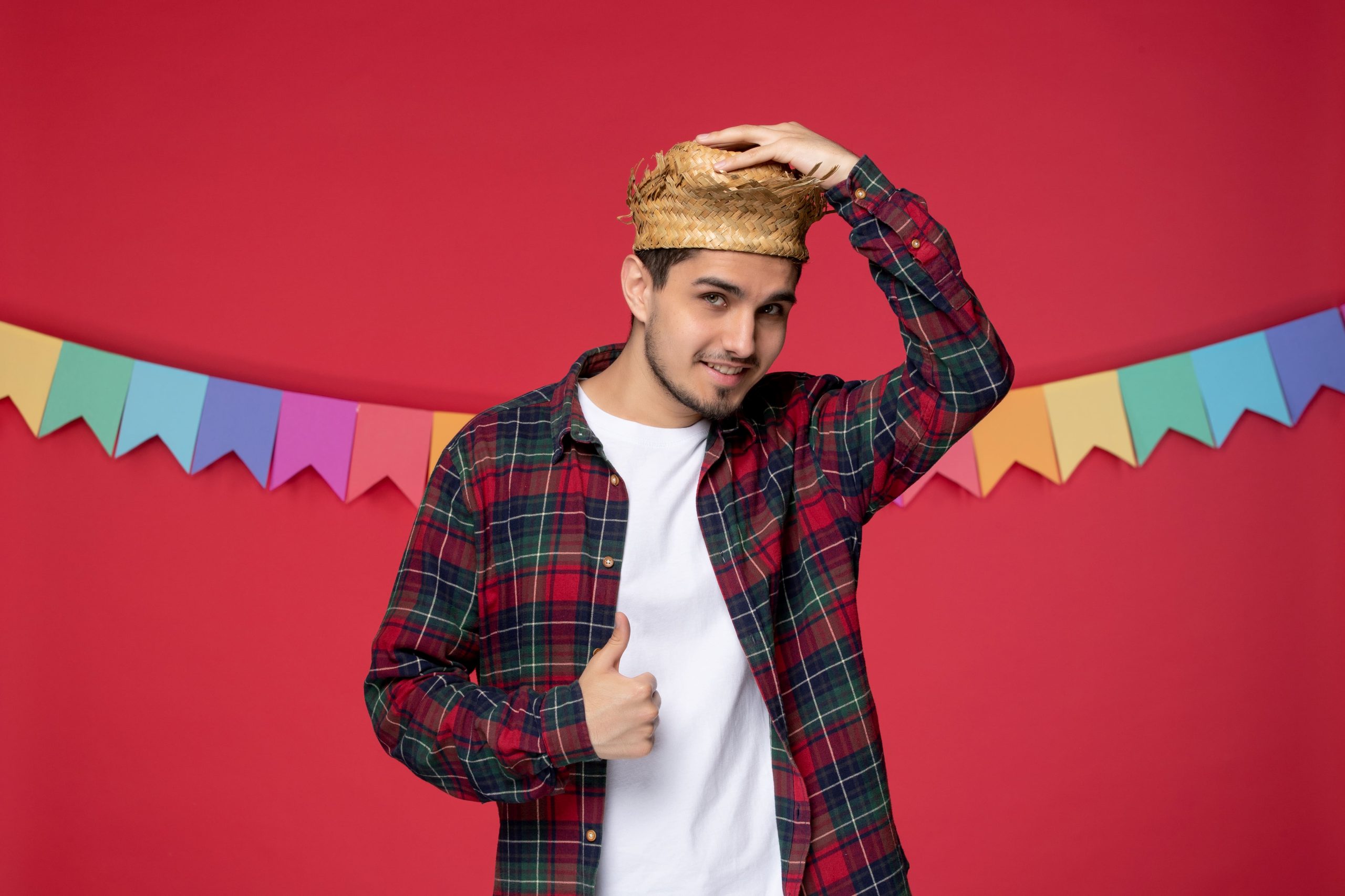 Homem com camisa xadrez e chapéu de palha em cenário decorado para festa junina.